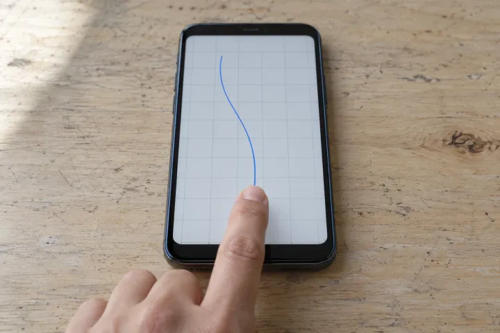 Finger tracing a plain grid on an unbranded handset at an inspection bench.
