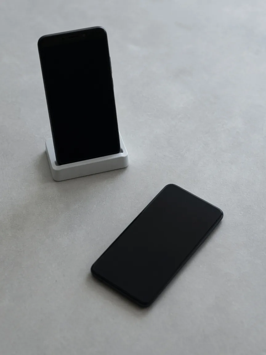 One dark phone stands in a light gray cradle and another lies flat. Both screens are black. The desk is bare and gray.
